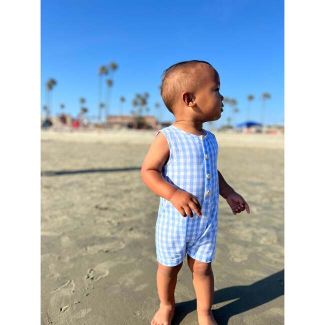 Toddler boy in blue and white sleeveless check romper with small wooden buttons. 